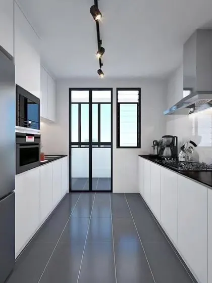 A minimalist parallel kitchen with clean lines, featuring all-white handleless cabinets and a contrasting black countertop. Track lighting on the ceiling ensures the entire narrow space is well-lit.