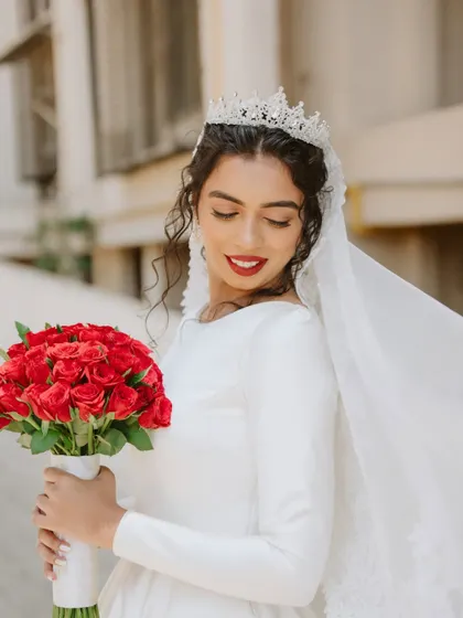 A close-up of her holding her bouquet. The red roses are a beautiful, classic choice that complements her bold red lip.