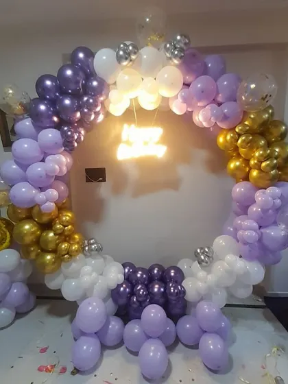 A 6th birthday balloon ring in purple, white, and gold, with a small neon initial in the center.