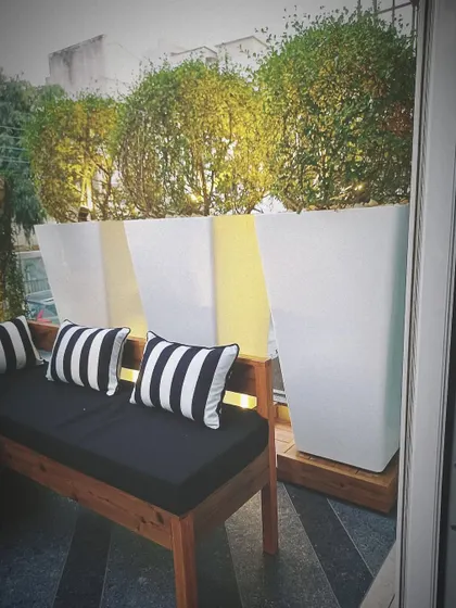 A close up of the balcony seating, with a wooden bench and black and white striped cushions. Behind it, tall white planters with topiaries create a clean, modern look.