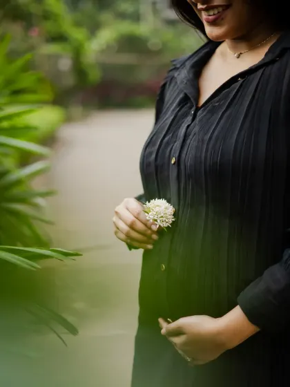 A close-up shot focusing on the baby bump, with the mother holding a small white flower. This artistic photo emphasizes the new life and delicate moments of pregnancy.