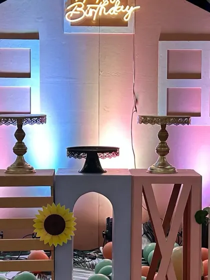 A dessert table area with a neon sign and modern, house-shaped shelving units, ready for cakes and treats.