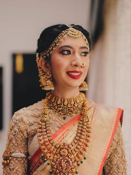 This bride looks beautiful and happy on her special day. Her off-white and gold saree with a custom embroidered blouse is a timeless choice.