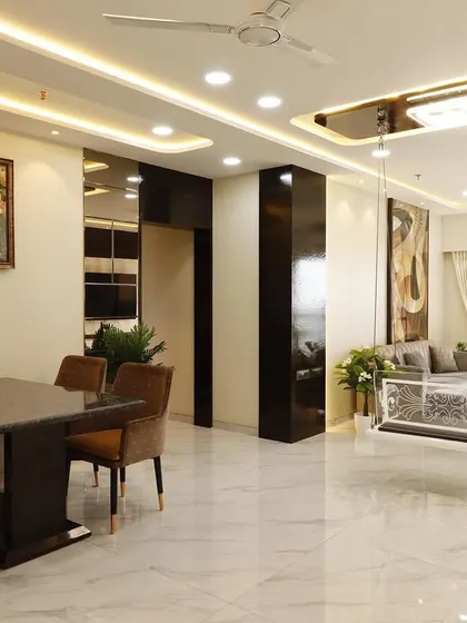 A wide-angle view of a completed 4BHK living room in Malad, featuring a central dining area and a separate lounge space with an acrylic swing. The glossy marble floors and extensive ceiling lights enhance the sense of luxury and space.