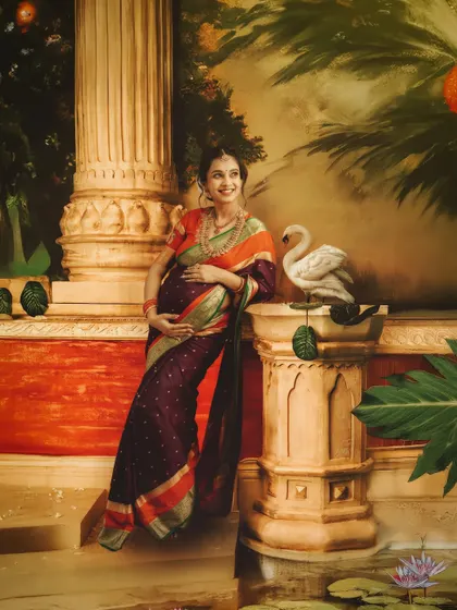 A serene portrait set against a painted backdrop of a palace garden. The mom-to-be leans against a pillar, creating a regal and artistic maternity image.