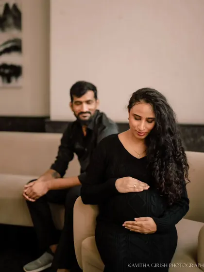 Another pose from the modern indoor shoot, focusing on the mother-to-be as she gazes down at her bump, with her partner watching over her from the background.