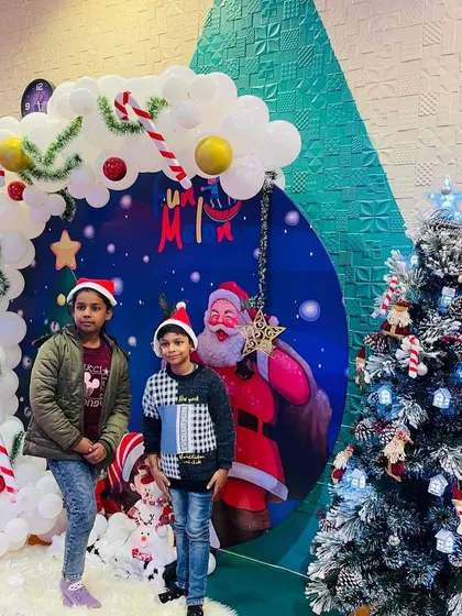 Two friends enjoying the Christmas festivities, wearing Santa hats and posing by the beautifully decorated tree.
