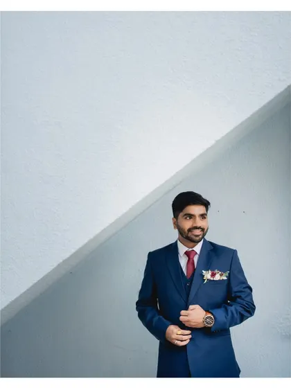 A minimalist portrait of the groom against a clean, white architectural background. The simple composition makes his blue suit pop.