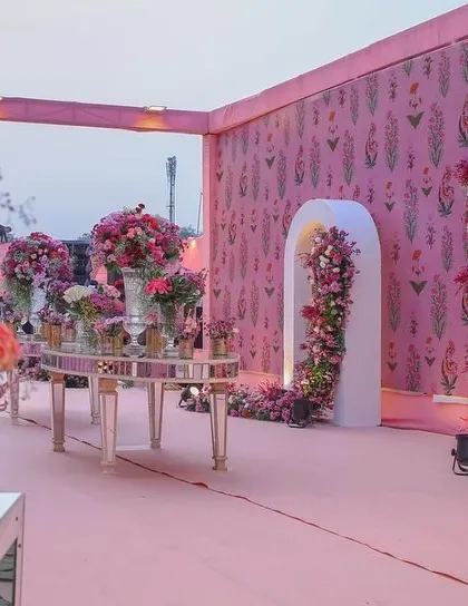 A beautiful pre-ceremony area near the mandap, decorated in pastel pink with floral arrangements and modern white arches.