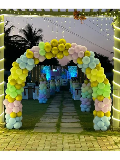 A breathtaking pastel rainbow balloon archway creating a grand entrance for an outdoor event. This welcoming decor piece, illuminated by string lights, sets a joyful and celebratory tone from the moment guests arrive.
