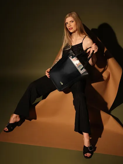 This shot captures a powerful and confident look, with the model directly engaging the camera. The pose showcases the handbag's structure and size, blending artistic direction with commercial appeal for a fashion brand.