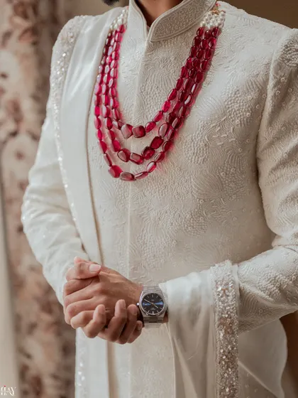 A close-up on the details of the groom's attire, from his textured white sherwani to his layered ruby necklace.