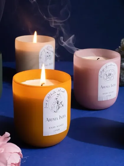 A collection of our frosted glass candles, their flames dancing among flowers. These luxury candles are designed to create a multi-sensory experience that helps you unwind, relax, and enjoy the moment.