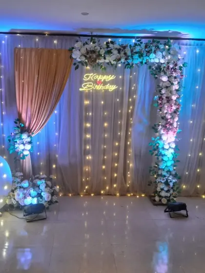 An elegant floral archway with a 'Happy Birthday' neon sign. The backdrop of fairy lights and drapes creates a magical and romantic setting for a special birthday.