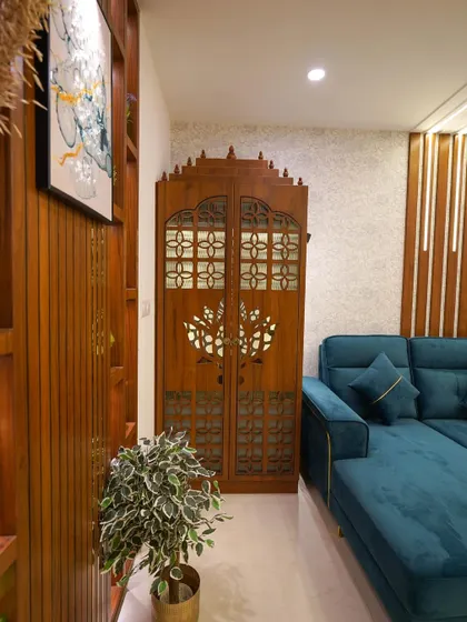 This living room corner showcases a beautifully crafted traditional pooja cabinet made of wood, seamlessly integrated next to a modern, comfortable L-shaped sofa.