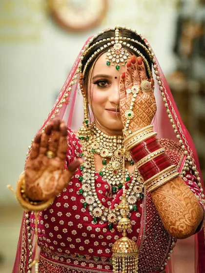 A playful and classic bridal pose. The bride peeks through her hands, showcasing her intricate mehndi design and her sparkling eyes, a perfect blend of tradition and personality.