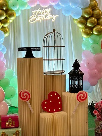 A dessert table setup for a candyland party, with decorative pedestals, a neon "Happy Birthday" sign, and sweet-themed props.