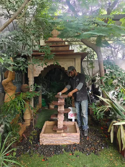 An artisan stands with the natural stone cascading fountain to show its scale. At 3 feet tall, it's a great mid-sized option for gardens.