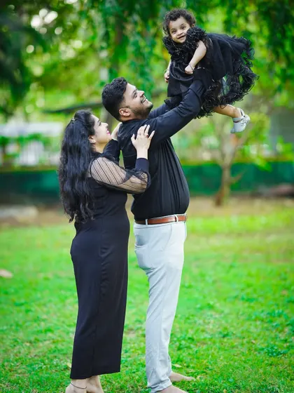 A father joyfully lifts his daughter into the air during a fun family photoshoot in the park.