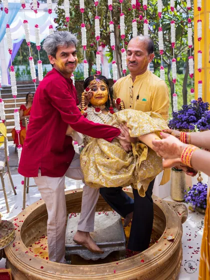 Family members lift the bride in a large traditional vessel (urli) during a unique and fun Haldi ritual.