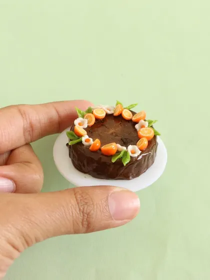 A close-up of the miniature chocolate fruit cake, held in hand to show its delicate size.