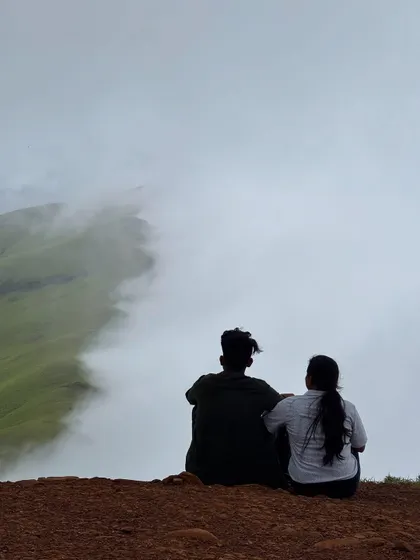 A couple enjoying the serene view from the top, as clouds gently kiss the mountainsides at Netravathi.
