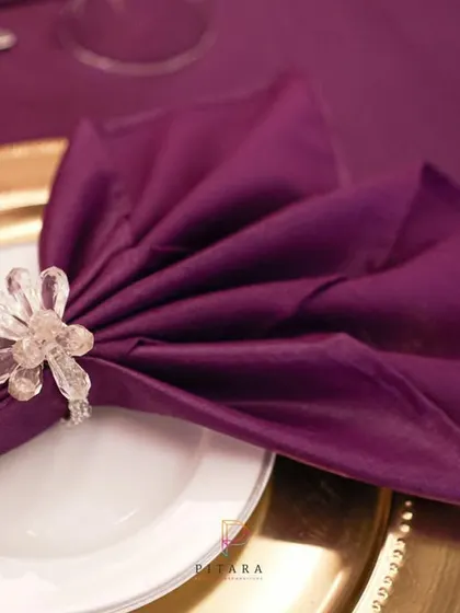 The beauty is in the details. A simple purple napkin is transformed with an elegant fold and a sparkling crystal napkin ring, sitting atop a gold charger plate.