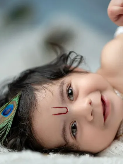 A playful and charming portrait of a baby boy dressed as Krishna. His sweet, curious expression and the peacock feather in his hair make this an unforgettable shot.