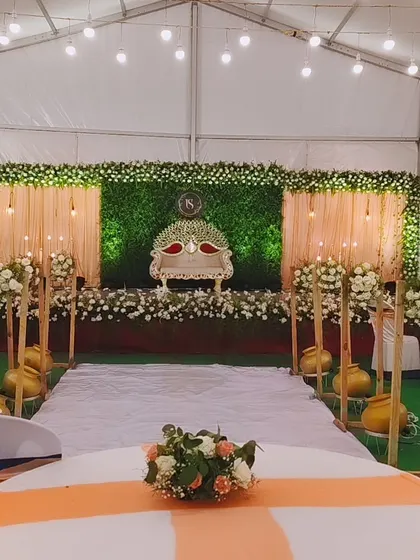 This reception stage setup in a tented venue features a lush green wall, elegant drapery, and beautiful floral arrangements, showing how I can transform any space.