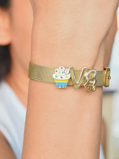 A custom name bracelet worn effortlessly. This piece spells out 'LOVE' with a cupcake charm, showing how you can mix letters and symbols for a unique look.