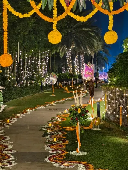 A stunning entrance and walkway for a large-scale outdoor Diwali party. We used extensive flower rangoli, hanging marigold garlands, and warm fairy lights to create a grand and welcoming path for guests.