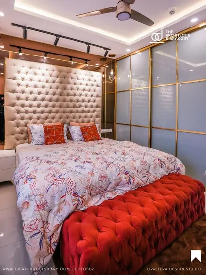 I believe a bedroom should be a personal sanctuary. For this master bedroom, I designed a floor-to-ceiling tufted headboard to create a sense of luxury, paired with a vibrant red ottoman for contrast. The lacquered glass wardrobe with gold accents adds a touch of glamour and provides ample storage.