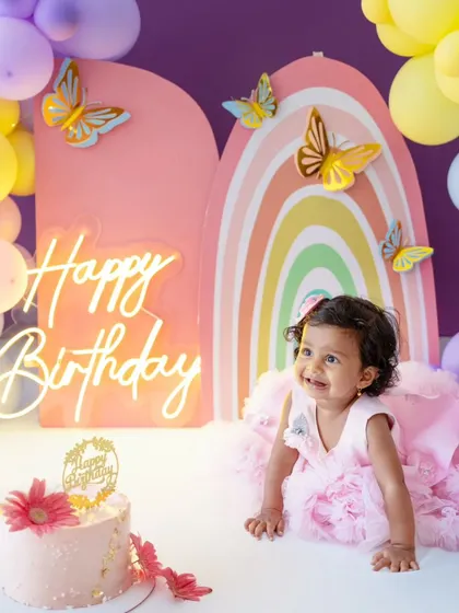 Crawling towards the cake with excitement! The pastel balloon arrangement and neon sign make this first birthday setup truly special.