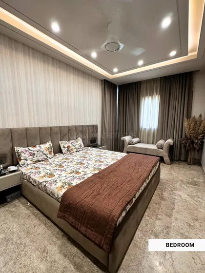 A beautifully designed bedroom in a neutral palette, featuring a comfortable bed with floral-patterned bedding and a chaise lounge for relaxation.
