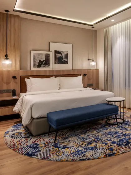 A guest room at Radisson Resort, Khopoli, where every design element is harmonized. The room features warm wooden flooring, statement pendant lights, and a striking blue circular carpet that anchors the space.