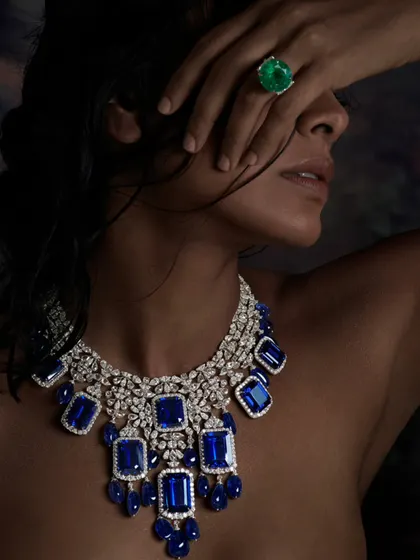A striking portrait featuring a magnificent sapphire and diamond necklace. The model's pose partially obscures her face, making the jewellery the undeniable hero of the image.