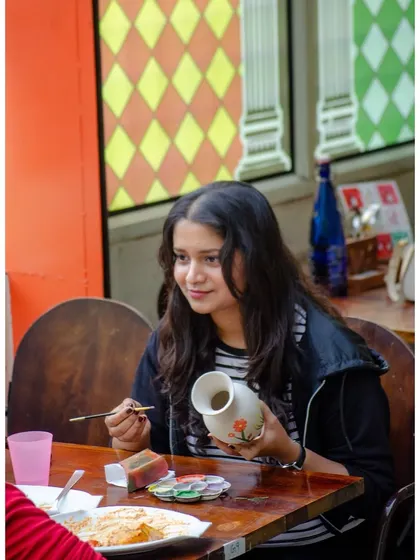 A guest smiles as she paints her ceramic vase, with a delicious meal on the table. This is what our paint and sip experience is all about.