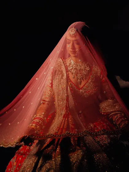 A beautiful, moody shot under the veil. The soft lighting highlights the shimmer on her eyelids and the delicate details of her bridal look.