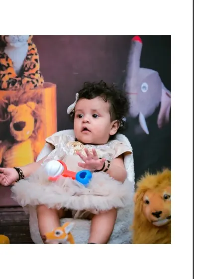 This baby girl looks on with a curious expression while holding a rattle during her jungle adventure shoot. The mix of colorful toys and plush animals makes the session engaging for her.