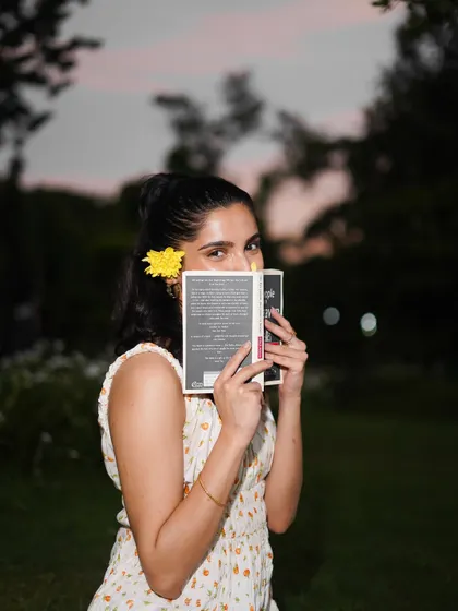 A playful peek over the book. The flower in her hair and the soft evening light add a touch of romance to this outdoor shot.
