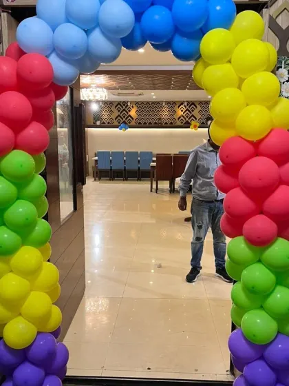 A vibrant rainbow-colored balloon arch at the entrance of a banquet hall for a birthday party.