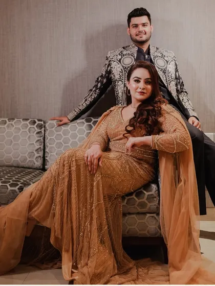 A relaxed yet regal portrait of the engaged couple. They are posed on a modern sofa, showcasing their elegant attire in a comfortable setting.