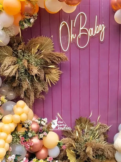 A detail shot of the baby shower backdrop, highlighting the texture of the purple wooden panel and the beautiful combination of the balloon garland and dried floral arrangements.