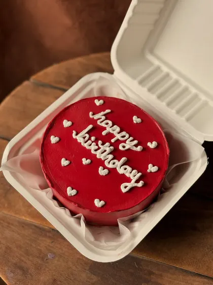 A vibrant red bento cake with "happy birthday" written in white cursive, surrounded by tiny white hearts. It's a simple yet striking design.