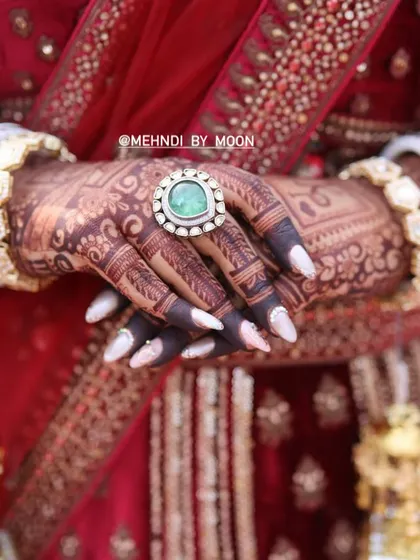 A close up shot focusing on the rich color of the henna stain. The dark color makes the intricate details of the finger designs and the large ring stand out beautifully.