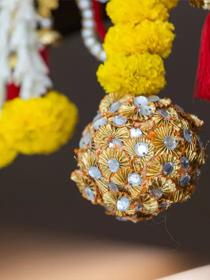 A close-up of a handcrafted gota patti ball, shimmering with sequins. These decorative spheres are hung from garlands, adding a touch of sparkle and festivity.