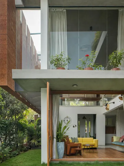 The architecture uses cantilevered slabs to create shaded outdoor spaces and balconies. This view shows the connection between the ground-floor living area and the upper-level bedroom, both opening to the greenery.