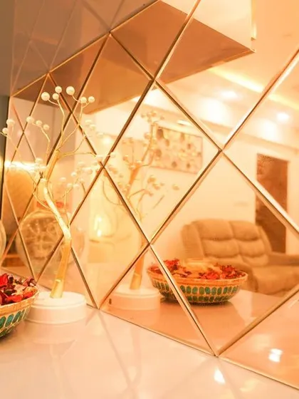 A detailed shot of the diamond-patterned bronze mirror backsplash on the crockery unit, reflecting the living room and adding a warm, decorative element to the space.