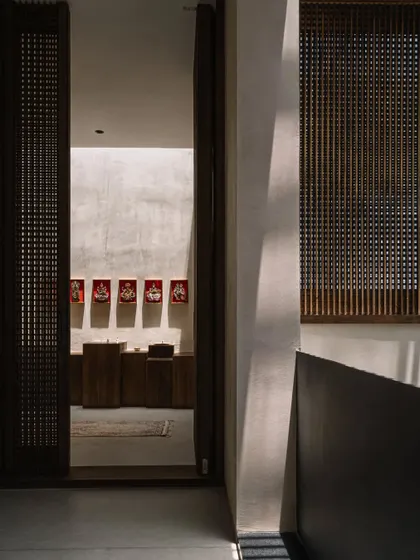 A view through a slatted wooden door into the serene puja room. The design emphasizes natural materials and a sense of tranquility, creating a spiritual corner within the home.