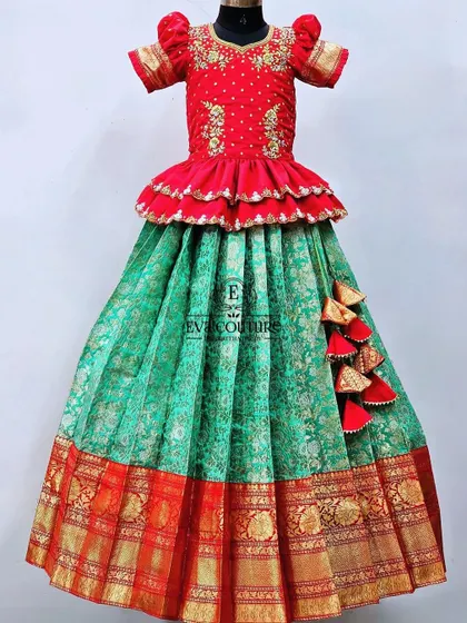 A beautiful Banarasi lehenga in red and green. The red peplum top has delicate embroidery, and the green skirt has a traditional red and gold border.